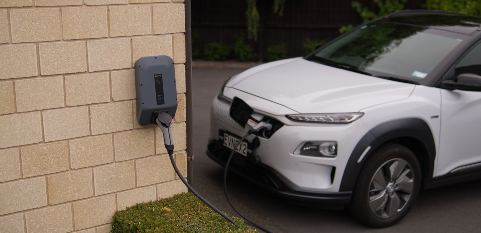 A white electric car charging on a wall-mounted EV charger in Pukekohe, New Zealand, showcasing modern eco-friendly transportation