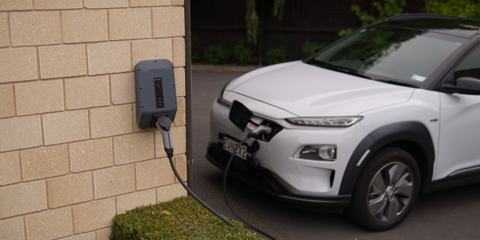A white electric car charging on a wall-mounted EV charger in Pukekohe, New Zealand, showcasing modern eco-friendly transportation