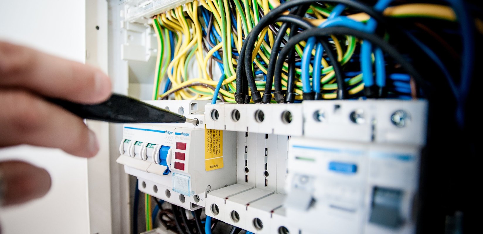Hand of electrician working on a circuit breaker panel with colorful wires, ensuring safe electrical connections