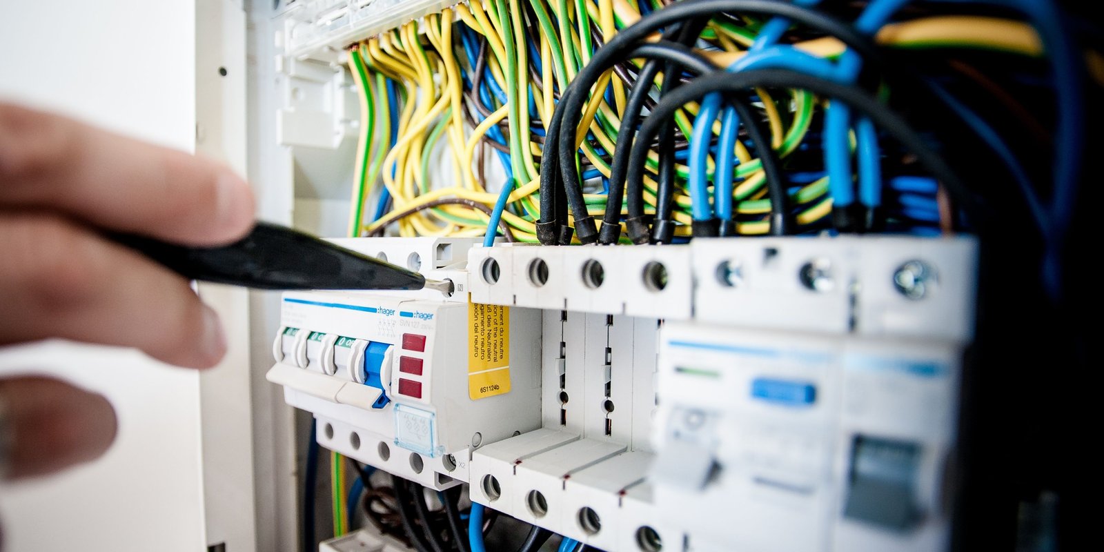 Hand of electrician working on a circuit breaker panel with colorful wires, ensuring safe electrical connections